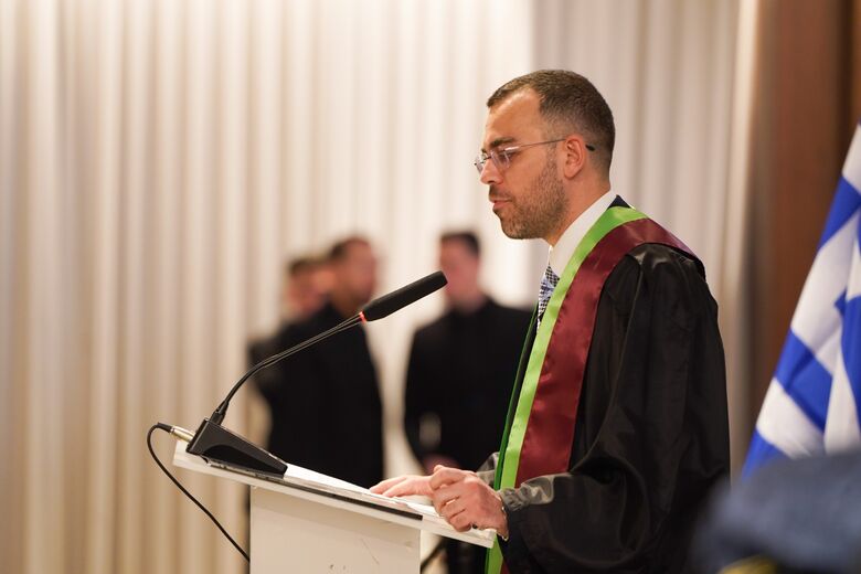 George Ntemos at the lectern during the ceremony, in academic dress, seen from the side.