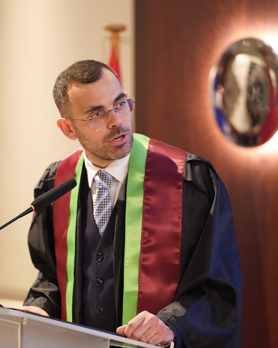 George Ntemos speaking at a lectern in academic dress.